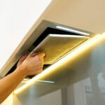 Person cleaning greasy range hood filter with baking soda and dish soap in kitchen sink