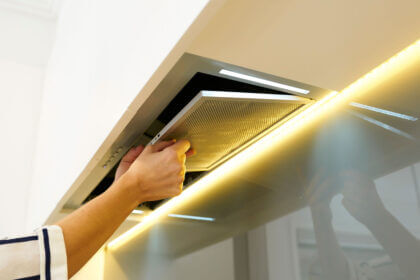 Person cleaning greasy range hood filter with baking soda and dish soap in kitchen sink