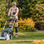 Person using lawn mower to cut grass at proper height following lawn mowing best practices for healthy yard
