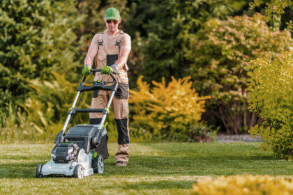 Person using lawn mower to cut grass at proper height following lawn mowing best practices for healthy yard