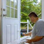 Person painting an exterior door with semi-gloss paint using proper brush technique for home improvement project