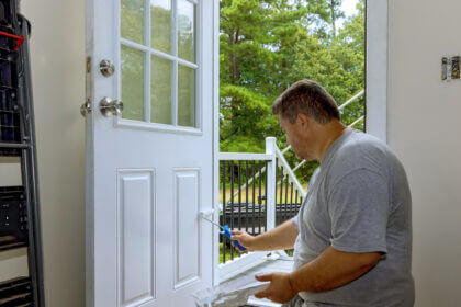 Person painting an exterior door with semi-gloss paint using proper brush technique for home improvement project