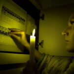 Homeowner checking electrical problems in house panel with flickering lights and hot outlets visible in background