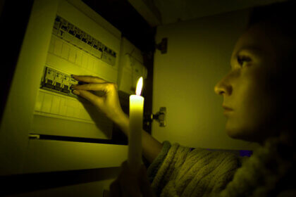 Homeowner checking electrical problems in house panel with flickering lights and hot outlets visible in background