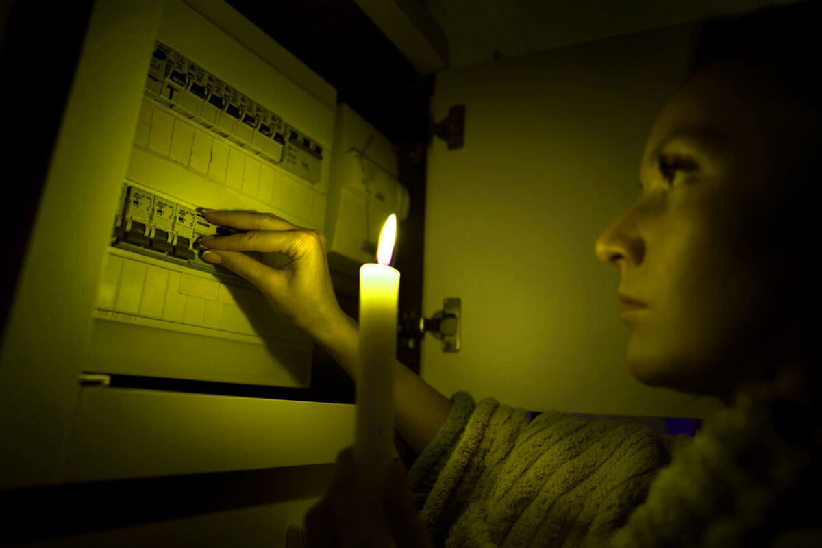 Homeowner checking electrical problems in house panel with flickering lights and hot outlets visible in background