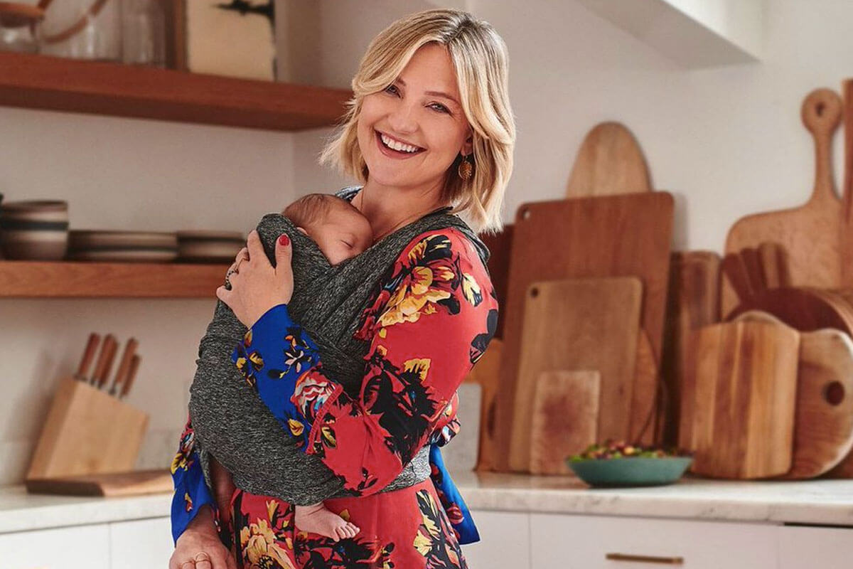 Kate Hudson kitchen with sage green cabinets, white countertops, and copper pot rack display above island