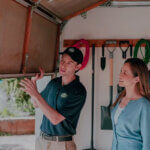 Professional technician performing garage door repair on residential overhead door with tools and safety equipment