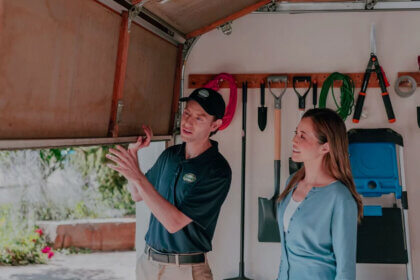 Professional technician performing garage door repair on residential overhead door with tools and safety equipment