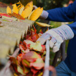 Homeowner following spring home maintenance tips checklist while inspecting house exterior and cleaning gutters