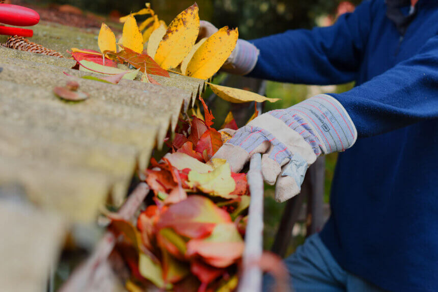 Homeowner following spring home maintenance tips checklist while inspecting house exterior and cleaning gutters