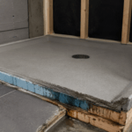pre slope shower pan base with visible water damage at edges and exposed wood framing in unfinished bathroom