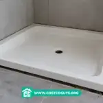 Tape measure across an acrylic shower pan checking width and depth before installation
