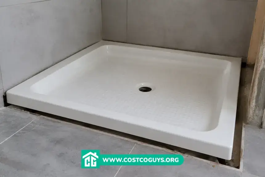 Tape measure across an acrylic shower pan checking width and depth before installation